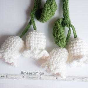 May include: A handmade crocheted garland featuring white lily of the valley flowers and green leaves. The garland is approximately 6 inches long.