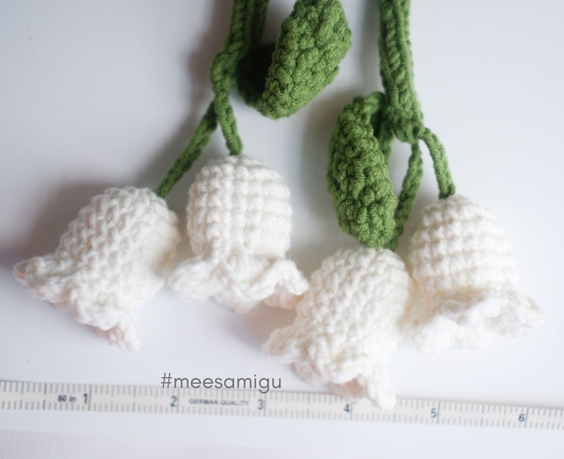 May include: A handmade crocheted garland featuring white lily of the valley flowers and green leaves. The garland is approximately 6 inches long.
