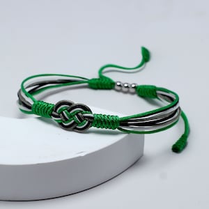 Könnte beinhalten: Ein geflochtenes Armband in Grün, Weiß und Schwarz mit einem silbernen Metallknoten. Das Armband hat einen verschiebbaren Knoten zum Anpassen der Größe.