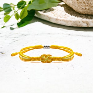 May include: A yellow and white braided bracelet with a knotted design and silver beads.