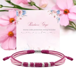 Puede incluir: Pulsera de cuerda trenzada rosa, blanca y plateada con una tarjeta que dice "Badass Gigi" y "pulsera de cuerda de protección en código morse".
