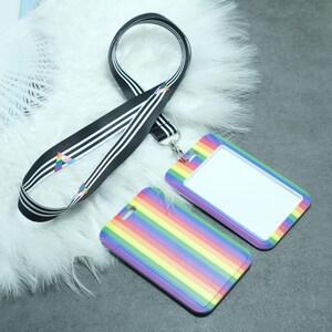 May include: A rainbow striped ID badge holder with a black and white striped lanyard. The badge holder has a clear plastic window for displaying an ID card.