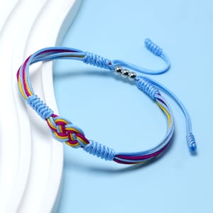 May include: A blue, pink and yellow braided friendship bracelet with silver beads. The bracelet has a knot design and is tied with a slip knot.