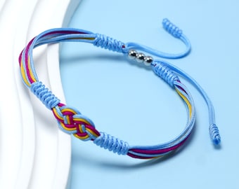 Puede incluir: Un brazalete de amistad trenzado azul, rosa y amarillo con cuentas plateadas. El brazalete tiene un diseño de nudo y está atado con un nudo corredizo.