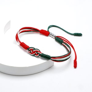 May include: A red, white and green braided bracelet with a silver bead accent. The bracelet is tied with a knot and has a long tassel.