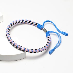 以下が含まれることがあります： ピンク、白、黒の織り糸と青い紐の端、銀色のビーズのアクセントが付いたブレスレット
