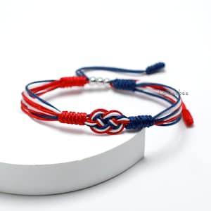 May include: Red, white, and blue braided friendship bracelet with a silver bead and a knot in the center.