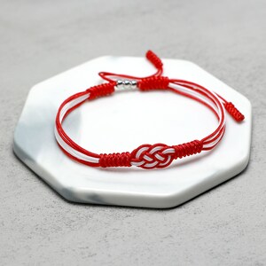 May include: Red and white braided bracelet with a silver bead and a knot in the center.
