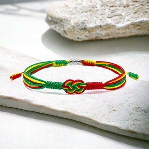 Puede incluir: Un brazalete trenzado rojo, amarillo y verde con un acento de cuentas plateadas y un diseño anudado.