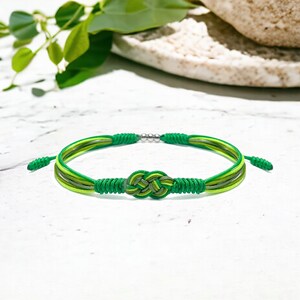 May include: A green and yellow braided bracelet with a knotted design. The bracelet is made of multiple strands of cord and has a silver bead.