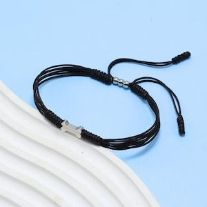 May include: Black adjustable bracelet featuring a silver-tone bone charm. The bracelet is made of multiple strands of black cord, with a sliding knot closure and three small silver beads. A simple, yet stylish accessory.