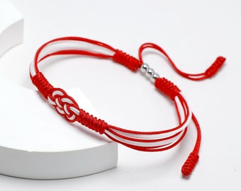 Puede incluir: Pulsera trenzada roja y blanca con un acento de cuentas plateadas. La pulsera está atada con un nudo.