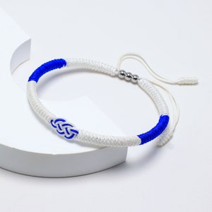 May include: A white and blue braided bracelet with a silver bead accent and a knotted design.