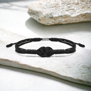 May include: A black braided bracelet with a knotted design and silver metal accents.