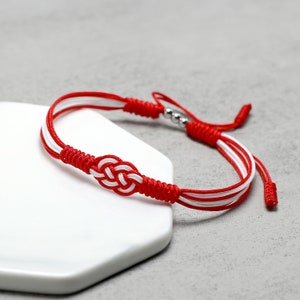 May include: Red and white braided bracelet with a silver bead and a knot in the center.