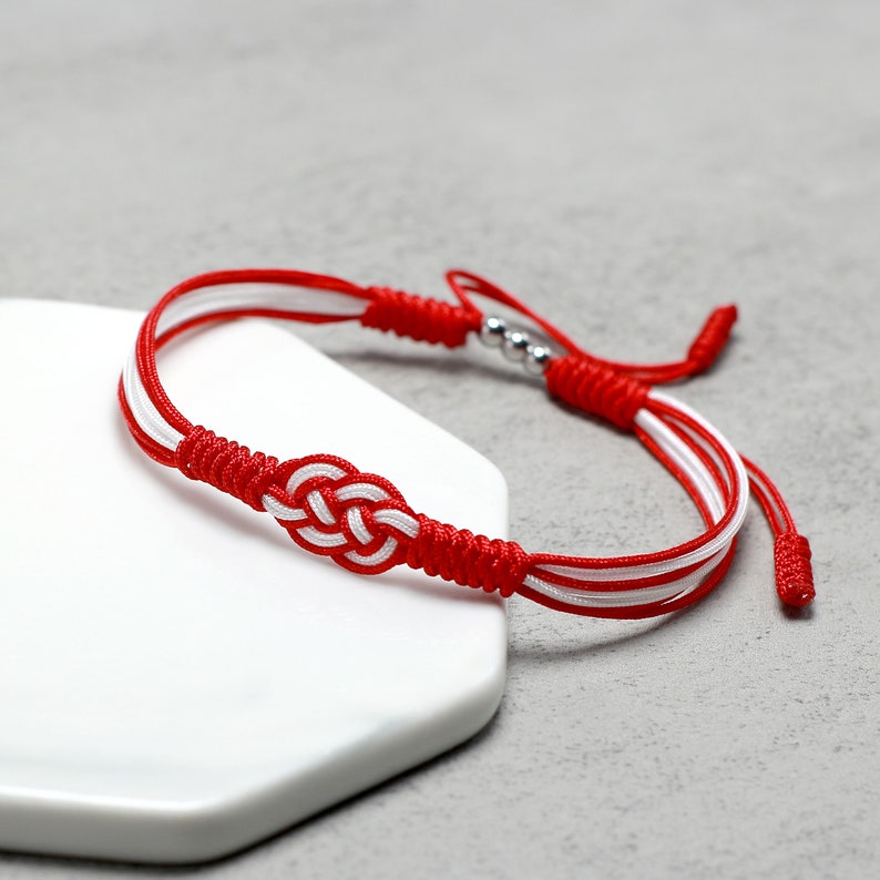 May include: Red and white braided bracelet with a silver bead and a knot in the center.