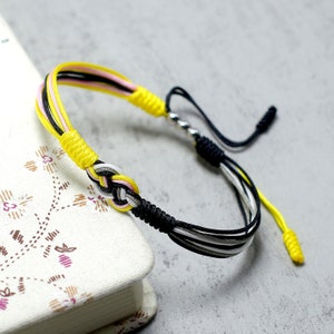 May include: A yellow, black and white braided bracelet with a silver bead and a knot in the centre.