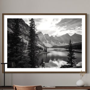 May include: Black and white photograph of a mountain lake with snow-capped peaks in the background. The lake is surrounded by trees and the water is calm and reflective.