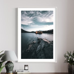 May include: A framed photograph of a lake with a small island in the distance. The lake is calm and the sky is cloudy. The island is covered in trees and there is a small building on it.
