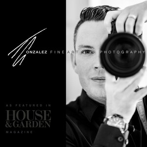May include: Black and white portrait of a photographer holding a camera to their eye. The photographer is wearing a black shirt and a watch. The text "GONZALEZ FINE ART PHOTOGRAPHY" is visible in the image. The text "AS FEATURED IN HOUSE & GARDEN MAGAZINE" is also visible in the image.