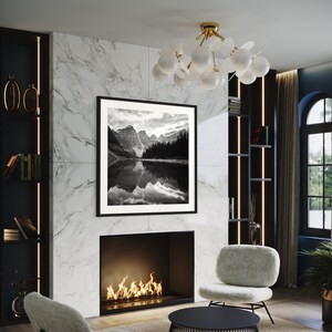 May include: A modern living room interior with a fireplace, two armchairs, a coffee table, and a black and white photograph of a mountain lake hanging on the wall. The room has a marble wall and a black and gold chandelier.