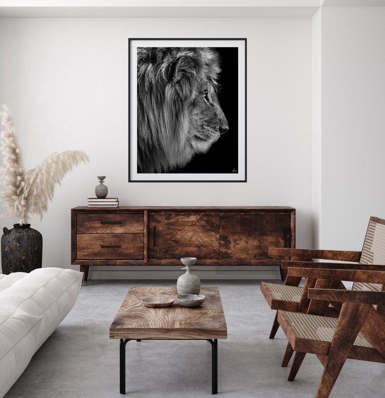 May include: A black and white photograph of a lion's profile, framed and hanging on a white wall above a wooden cabinet. The lion is looking to the right, with its mane flowing in the wind. The photo is set against a dark background.