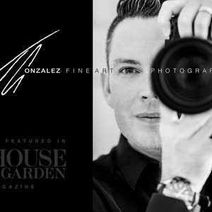 May include: Black and white photo of a photographer holding a camera up to their face. The text "GONZALEZ FINE ART PHOTOGRAPHY" is visible in the background. The text "AS FEATURED IN HOUSE & GARDEN MAGAZINE" is also visible in the background.
