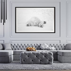 May include: A gray sectional sofa with tufted upholstery and a matching gray ottoman. The sofa is positioned in front of a black framed photograph of a polar bear lying on its back in the snow.