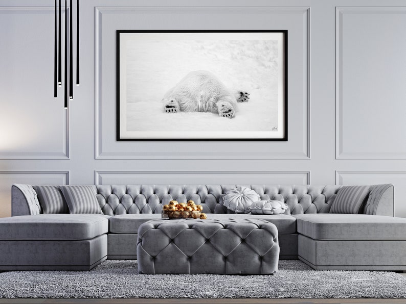 May include: A gray sectional sofa with tufted upholstery and a matching gray ottoman. The sofa is positioned in front of a black framed photograph of a polar bear lying on its back in the snow.