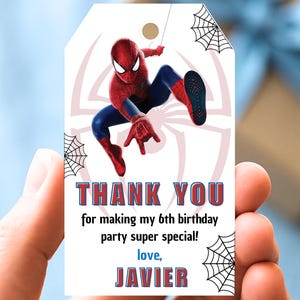 May include: A white gift tag featuring Spider-Man in a dynamic pose, with a pink spider web design. The tag includes the text "THANK YOU" and a personalized message for a 6th birthday party, signed "Javier".