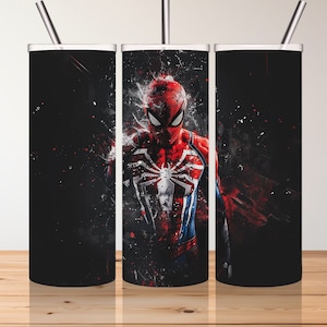 Puede incluir: Tres vasos de acero inoxidable con tapas y pajitas. Los vasos son negros con un gr&aacute;fico de Spider-Man con un traje rojo y azul con un s&iacute;mbolo de ara&ntilde;a negro en el pecho. El fondo es un patr&oacute;n de salpicaduras negro y rojo.