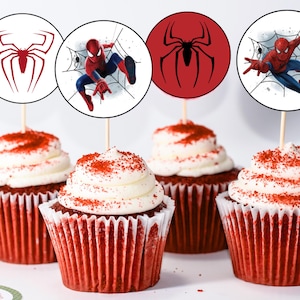 K&ouml;nnte beinhalten: Vier rote Samt-Cupcakes mit wei&szlig;em Frosting und roten Streuseln, die mit runden Papier-Cupcake-Toppern verziert sind, die einen Comic-Spiderman-Charakter und ein rotes Spinnennetz-Design zeigen.