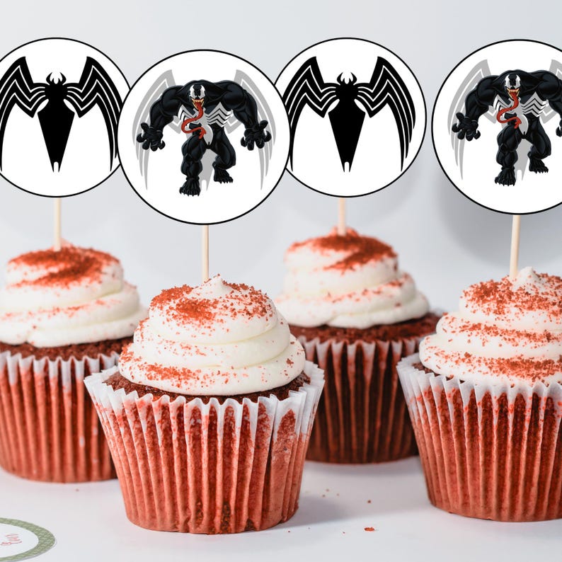 May include: Four red velvet cupcakes with white frosting and red sprinkles topped with round paper cupcake toppers featuring a black and white cartoon image of Venom from the Marvel comics.