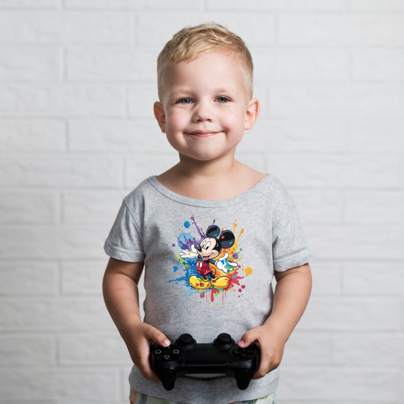 May include: A young boy wearing a grey t-shirt with a colorful Mickey Mouse graphic. He is holding a black video game controller.