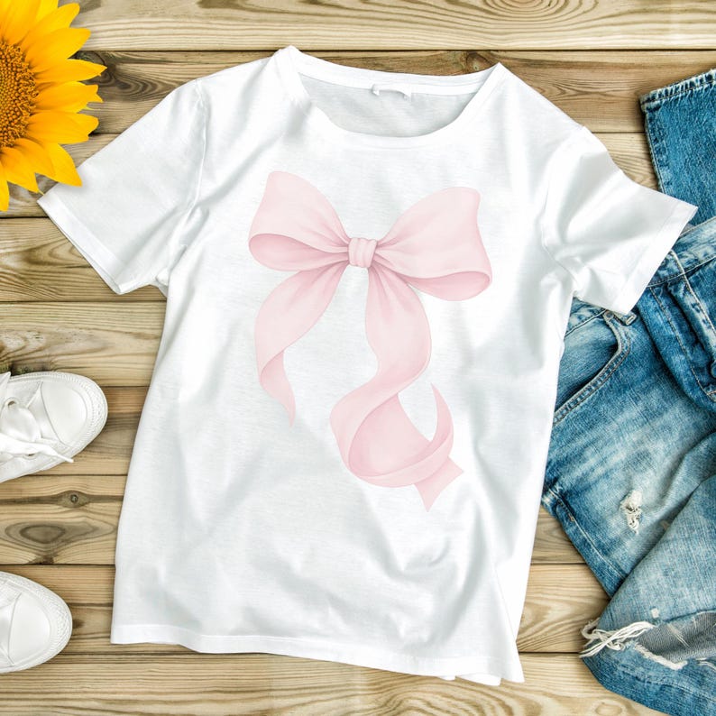 Peut inclure: T-shirt blanc avec une illustration &agrave; l'aquarelle d'un n&oelig;ud rose. Le n&oelig;ud a des rubans fluides et est centr&eacute; sur le t-shirt. Le t-shirt est associ&eacute; &agrave; un jean bleu et &agrave; des baskets blanches, sugg&eacute;rant une tenue d&eacute;contract&eacute;e.