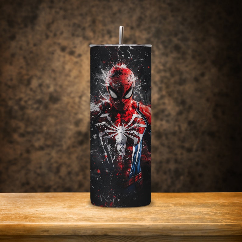 Puede incluir: Un vaso de acero inoxidable negro y rojo con un gr&aacute;fico de Spider-Man en un traje rojo y azul con un logotipo de ara&ntilde;a negro en el pecho. El fondo es negro con salpicaduras de pintura blanca.