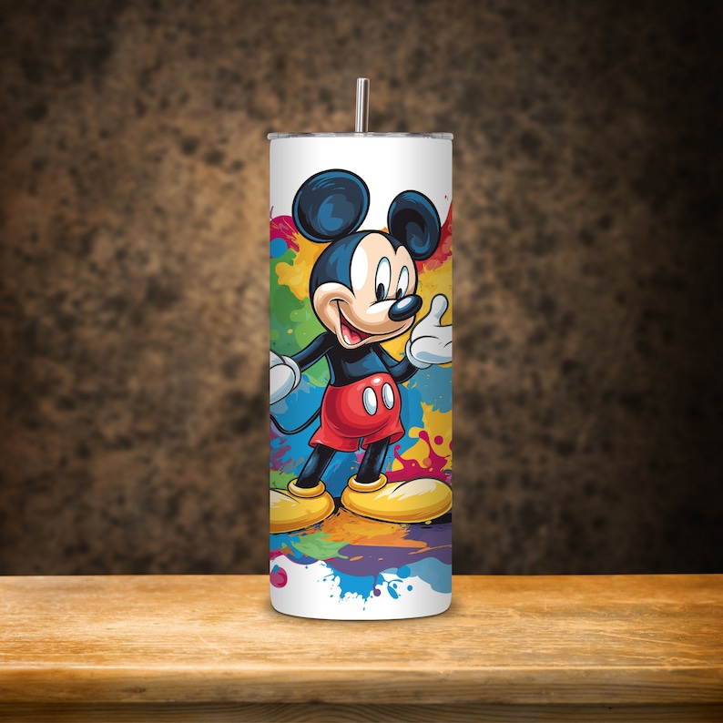 May include: A white stainless steel tumbler with a colourful paint splatter design featuring Mickey Mouse. Mickey Mouse is wearing red shorts and yellow shoes.