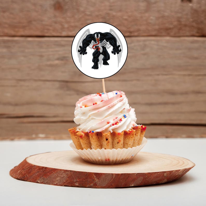May include: A cupcake with pink and white frosting and colorful sprinkles topped with a round white cake topper featuring a black and white illustration of Venom, a Marvel Comics superhero.