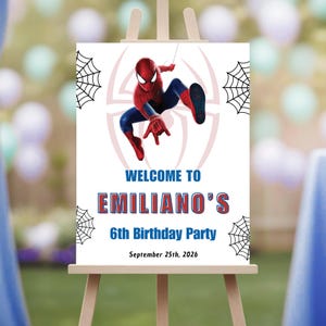 Op de afbeelding: Een wit bord op een houten ezel met een Spider-Man-afbeelding. Op het bord staat "WELCOME TO EMILIANO'S 6th Birthday Party" met de datum "September 25th, 2026". Spinnenwebben staan in de hoeken.