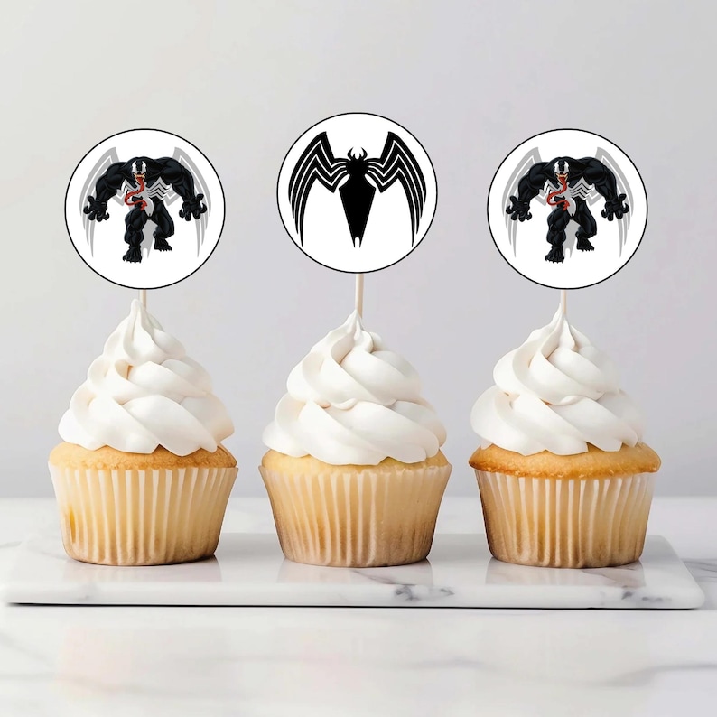 May include: Three cupcakes with white frosting topped with round edible paper cupcake toppers featuring a black and white image of Venom, a Marvel Comics superhero.