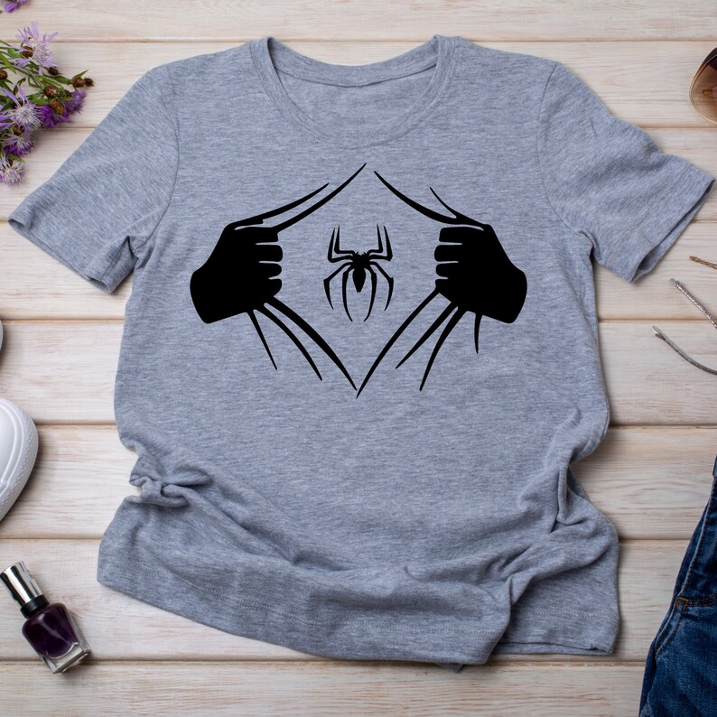 Puede incluir: Una camiseta gris con un gr&aacute;fico negro de una ara&ntilde;a que sale de la camiseta. La ara&ntilde;a est&aacute; en el centro del gr&aacute;fico y tiene ocho patas.