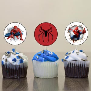 K&ouml;nnte beinhalten: Drei Cupcakes, verziert mit rotem, wei&szlig;em und blauem Frosting. Jeder Cupcake hat einen runden, essbaren Topper mit einem anderen Bild von Spiderman. Ein Topper zeigt Spiderman in einem Netz, ein anderer zeigt Spiderman in einem rot-schwarzen Anzug und der letzte Topper zeigt Spiderman in einem rot-blauen Anzug.