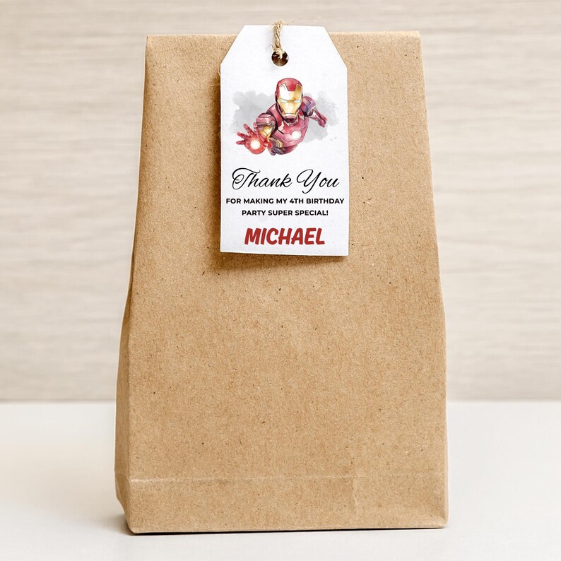 May include: A brown paper gift bag with a white tag. The tag features an Iron Man illustration and the text "Thank You" and "Michael". The tag is attached with a natural twine.