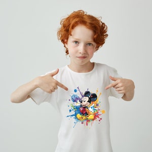 May include: A white t-shirt with a colorful paint splatter design featuring Mickey Mouse in the center. Mickey Mouse is wearing red shorts and yellow shoes.