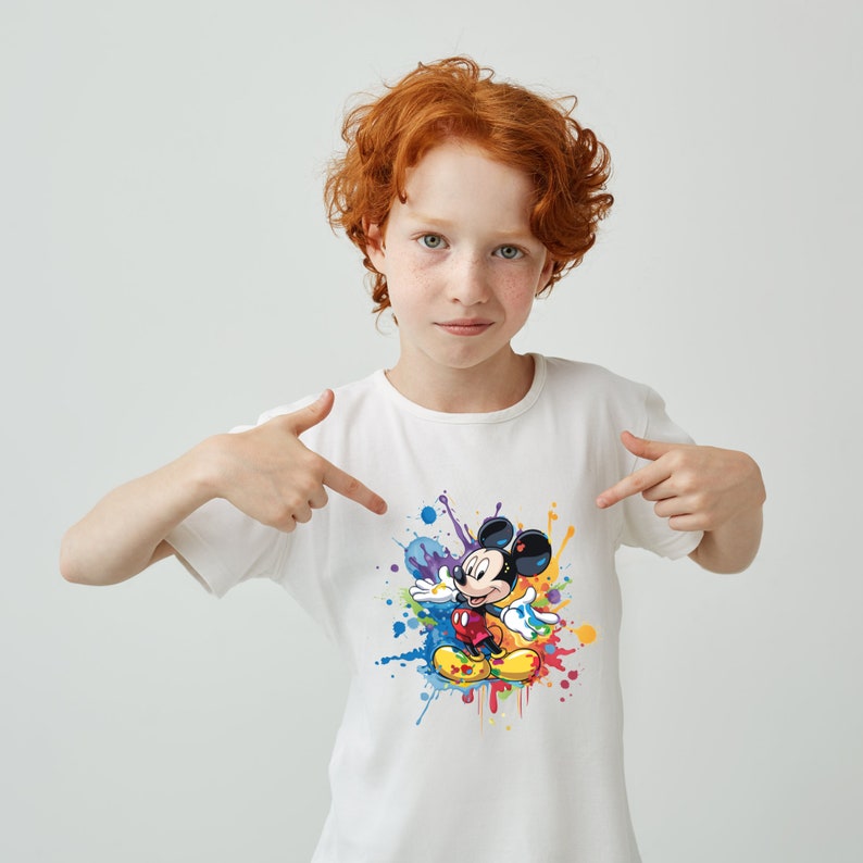 May include: A white t-shirt with a colorful paint splatter design featuring Mickey Mouse in the center. Mickey Mouse is wearing red shorts and yellow shoes.