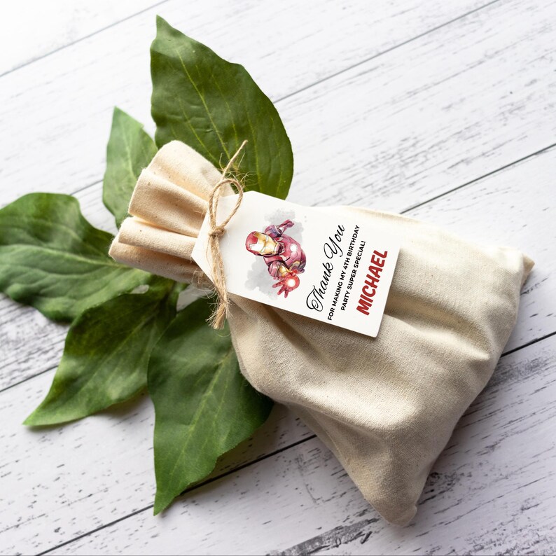 May include: A beige fabric gift bag with a tag tied with twine. The tag features an Iron Man illustration and the text "Thank You" and "MICHAEL". Green leaves are in the background.