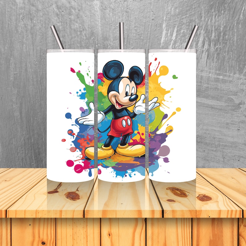 May include: Three white stainless steel tumblers with Mickey Mouse in a colourful paint splatter design. The tumblers have lids and straws.