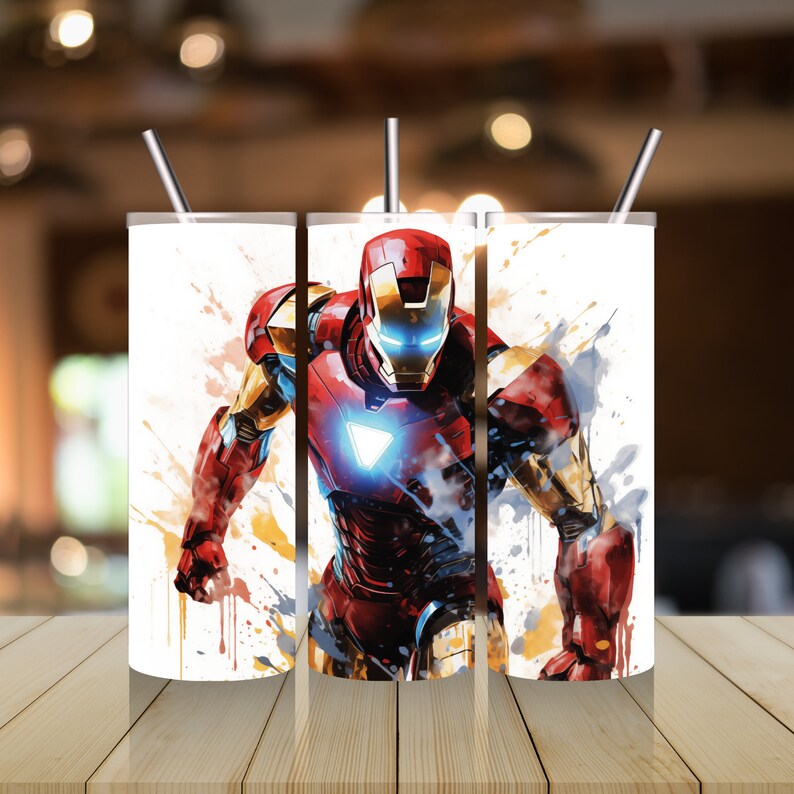 Op de afbeelding: Drie roestvrijstalen bekers met een witte achtergrond en een kleurrijk beeld van Iron Man in een superheldenpose. Het beeld heeft een aquareleffect met spatten van gele, oranje, rode en blauwe verf.