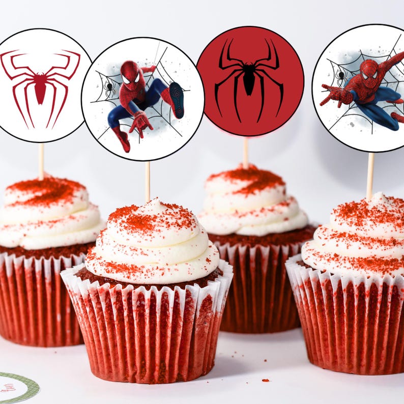 K&ouml;nnte beinhalten: Vier rote Samt-Cupcakes mit wei&szlig;em Frosting und roten Streuseln, die mit runden Papier-Cupcake-Toppern verziert sind, die einen Comic-Spiderman-Charakter und ein rotes Spinnennetz-Design zeigen.