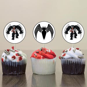 May include: Three cupcakes decorated with red and white frosting and topped with silver sprinkles. Each cupcake has a round, white paper topper with a black and white image of the superhero Venom.